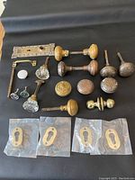 Full collection of various antique and vintage door knobs, keyhole covers, plates and hardware laid out on black background showing variety and condition.