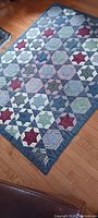 Full view of vintage handmade star pattern quilt laid flat on wooden floor showing multicolored star blocks and patchwork squares