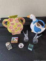 Image showing handmade ceramic vase with floral rose motif, ceramic mother goose pitcher, pair of glass swan figurines, small Mexican wall ornament, and clear crystal decorative pieces including a teal glass piece.