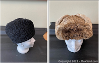Two women's vintage winter hats displayed side by side on mannequin heads: a black curly lambs wool cap and a light brown rabbit fur hat with ear flaps.