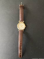 Full view of the Seiko women's wristwatch with round gold-tone case and brown leather strap laid flat on black surface.