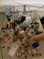 Overview of the animal figurines collection showing various animals arranged on a table, including glass, ceramic, porcelain, and plastic pieces.