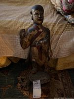 Front view of wooden statue showing person standing on base with raised hand and chipping paint