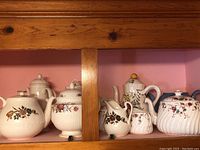 Wooden shelf display with multiple bone china pots and accessories with floral patterns, showing various shapes and sizes.