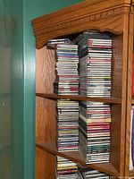 Five shelves in a wooden corner shelf unit filled with stacks of CD cases, showing a large number of compact discs primarily classical music.