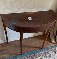 Full view of semi-circular wooden demilune table with straight tapered legs and visible surface wear.