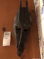 Front view of the wooden ethnic mask showing the two vertical ridged horns, dot pattern decoration, eye openings, and overall shape.