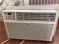 Front view of GE window air conditioner installed in a window with visible vent grille and control panel.