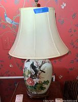 Front view of ginger jar lamp showing its ceramic body with painted birds and flowers, shade and fruitwood base.