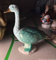 Herend turquoise green goose figurine showing side profile with gold accented wings and beak.