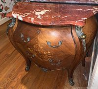 Front and side view of the Bombay chest showing curved wood inlay design with floral pattern, red marble top and metal hardware on drawers and corners.