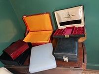 Photo showing six assorted jewelry boxes on a wooden surface against a green wall.