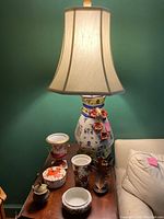 Photo showing assortment with the ceramic lamp with floral decor and fabric shade, various vases, and a covered dish on a wooden table