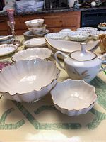 Wide angle showing seven Lenox porcelain serving bowls and a covered sugar bowl with gold trim on a table.