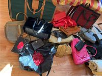 Overview of assorted bags and suitcases including black patent faux fur handbag, red and pink handbags, and several travel bags in varied colors
