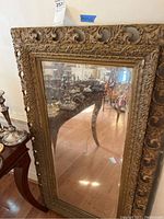 Full view of the rectangular mirror showing the detailed gold ornate frame and reflection.
