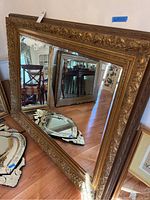 Large vintage mirror with gold ornate frame standing against a wall, showing full size and adjacent decorative mirrors.