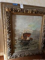 Frontal view of oil painting in ornate carved frame showing sailboats on choppy water with red sail