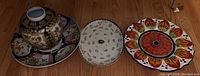 Photo of three pieces: round Satsuma style vase on a coordinating platter, white round platter with floral design, and bright Imari style plate.