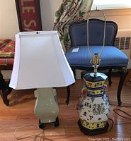 Photo showing both lamps: one with white hexagonal fabric shade, other with exposed ceramic body and no shade, both with wooden bases on hardwood floor.