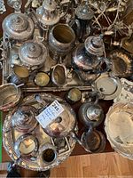 Top down view of multiple silver-plated tea and coffee servers, creamers, sugar bowls, and trays showing tarnish and ornate handles.