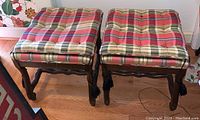 Two upholstered stools with Chinoiserie wooden frames, plaid cushions, tassels, positioned side by side on hardwood floor
