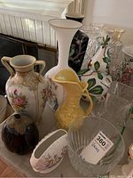 A collection of various vases made of glass and ceramic with different shapes, colors, and floral patterns on a table.