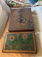 Closed view of the paint carved wooden box with floral detail bottom and Asian writing on top lid.