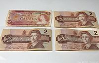 Four Canadian two-dollar bills laid out together, showing one older pink-style bill and three 1966 brown-style bills.