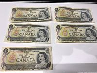 Five old Canadian one dollar bills laid out showing fronts with Queen Elizabeth II and bilingual text.