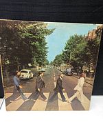Front cover of The Beatles Abbey Road album showing the four band members walking across a zebra crossing on a street.