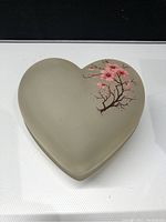 Heart-shaped frosted glass box with pink floral blossom design visible on the lid, showing the front and top views.