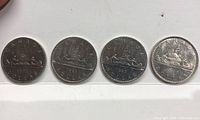 Four Canadian one-dollar coins featuring the Voyageur design with dates 1973, 1981, 1982, and 1985 visible.