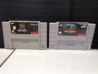 Two gray Super Nintendo cartridges side by side, labeled Mortal Kombat 3 and Mortal Kombat 2, showing front labels with game logos and some wear.