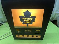 Front view of vintage Toronto Maple Leafs wall light illuminated showing the maple leaf logo and scoreboard with home and visitor scores and digital time display
