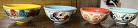 Four hand painted mini bowls displayed side by side on a wooden surface, showing the external floral designs and colors.