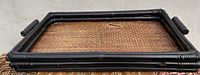Photo of a rectangular woven basket with a black wooden or bamboo frame and handles on the shorter sides.