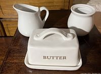 Photo showing butter dish, creamer, and sugar bowl placed on wooden surface
