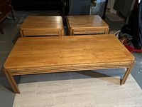 Photo showing rectangular wooden coffee table and two matching square end tables with rounded edges and consistent wood finish.