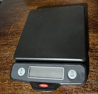 Black OXO digital food scale showing top surface with weighing platform, LCD screen, power and unit buttons