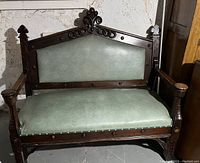 Front view of heavy solid wooden bench showing ornate carved backrest and green upholstery on seat and backrest
