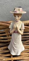 Front view of the porcelain ceramic lady figurine with hat and long dress, showing painted details and facial expression.