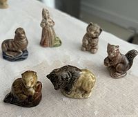 Six assorted Wade ceramic figurines on a white fabric background including animals and a human figure.