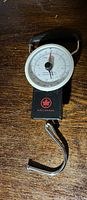 Mechanical luggage scale featuring a white dial, black casing, metal hook and Air Canada logo on black base.