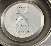 Close-up image inside the metal container showing the text 'SHARON OSBOURNE COLON CANCER PROGRAM' with a large ampersand symbol.