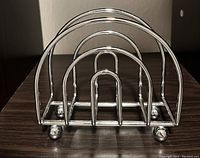 Photo of a shiny chrome metal napkin holder with a curved design and four rounded feet on a dark wooden surface.