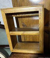 Photo of the solid wood rectangular wall shelf showing its two interior shelves and natural wood grain finish.