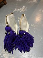 Off-white cowgirl boots showing purple yarn tassels with silver metal beads on the front.