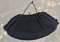 Photo of a vintage black fabric evening purse with metal clasp and short chain handle against a concrete-like background.