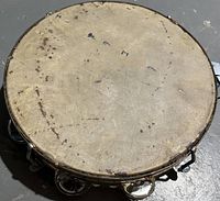 Top view of vintage tambourine showing natural skin drumhead with signs of wear and handwritten numbers/letters.